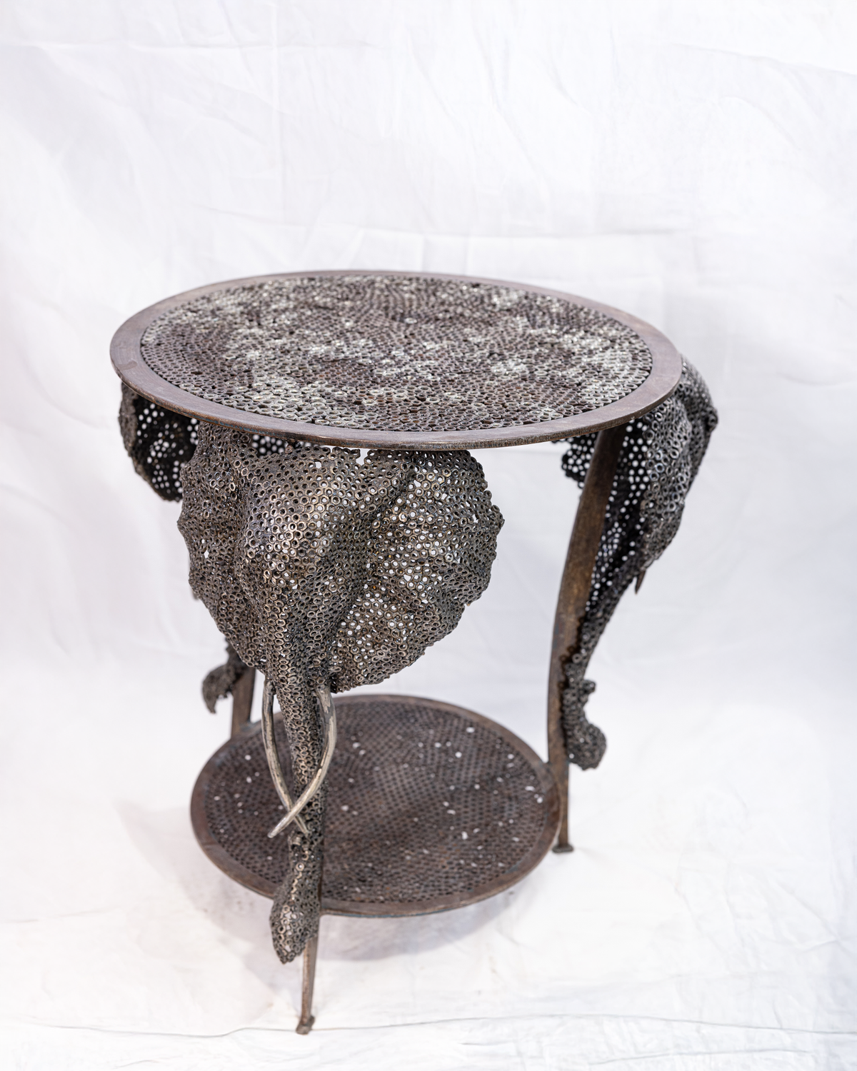 A fully functional square side table with legs structured and embellished by welded iron nuts forming three elephant heads, set against a plain background.