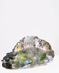 A handmade ceramic sculpture of a large fish with a wide, rounded body and an open mouth, glazed in a distinctive bubbled cellular pattern of olive green, yellow-green, pale blue, and dark grey, set against a plain white background.