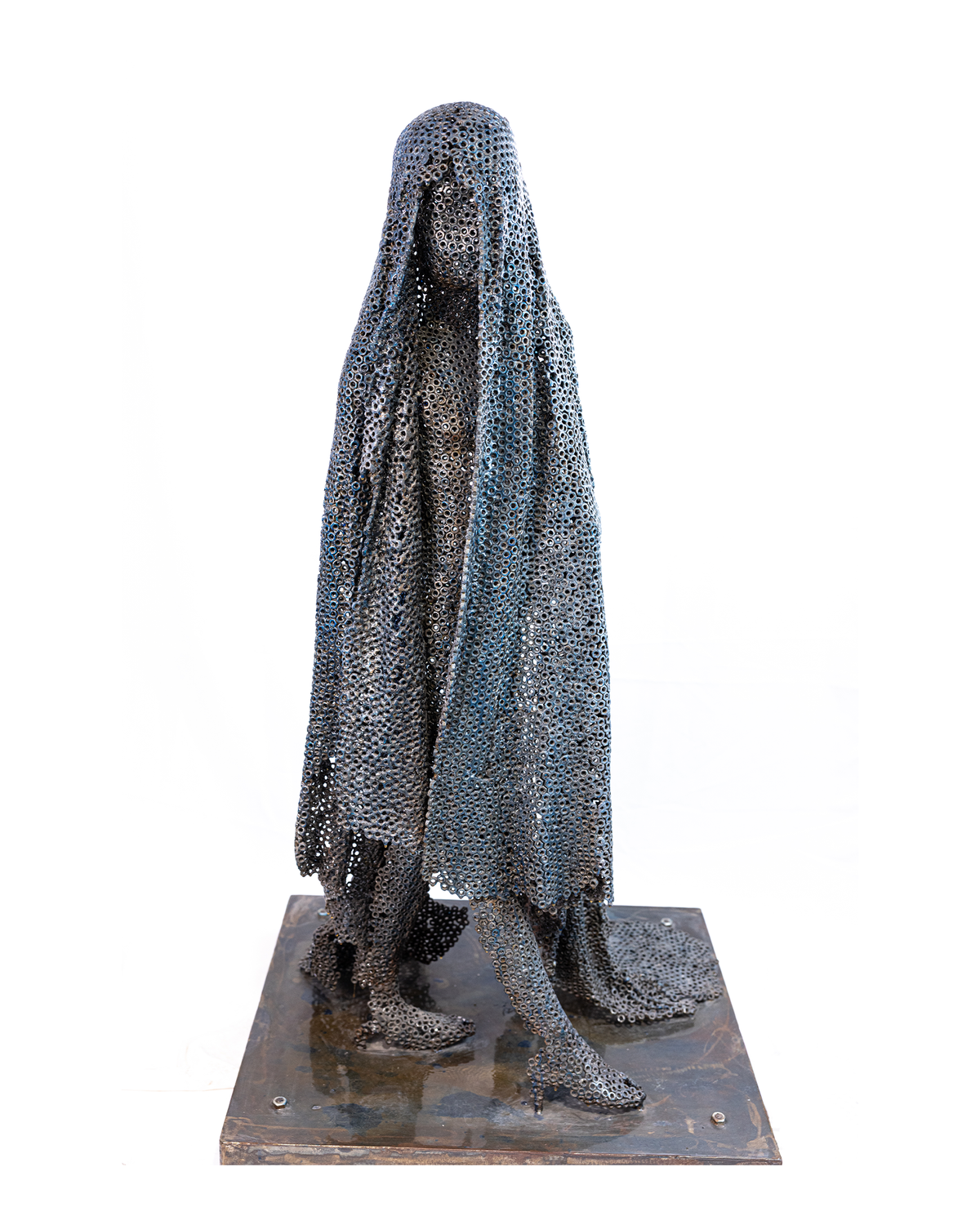 A life-sized figurative sculpture of a solitary draped figure with a cascading veil and hidden face, constructed entirely from a lattice of welded dark iron nuts that falls like fabric frozen in time, standing on a dark metallic base against a plain white background.