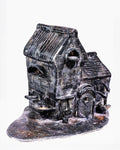 A handcrafted ceramic sculpture titled "Dream," featuring a detailed miniature brick building with a dark black and grey glaze, accented by white highlights across its textured brickwork and ribbed pitched roof, set against a white background.