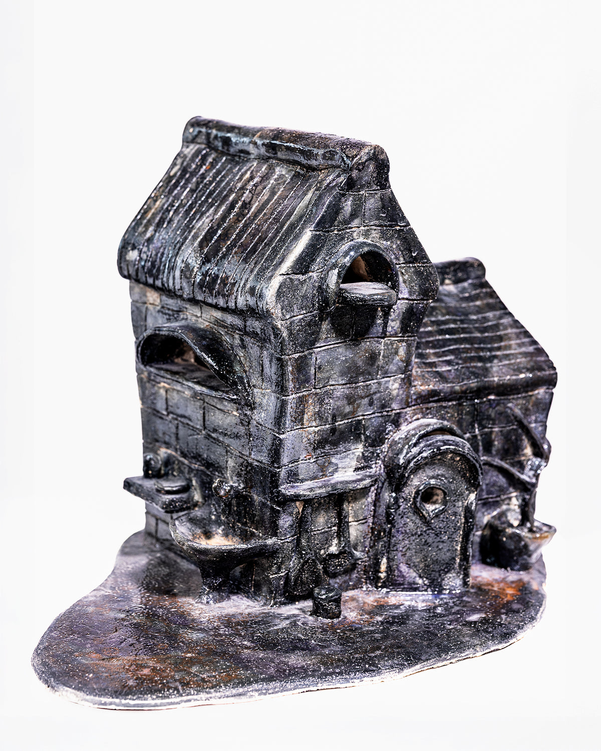 A handcrafted ceramic sculpture titled "Dream," featuring a detailed miniature brick building with a dark black and grey glaze, accented by white highlights across its textured brickwork and ribbed pitched roof, set against a white background.