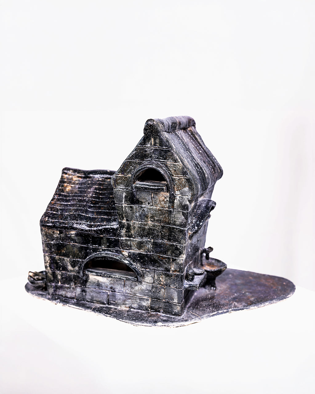 A handcrafted ceramic sculpture titled "Dream," featuring a detailed miniature brick building with a dark black and grey glaze, accented by white highlights across its textured brickwork and ribbed pitched roof, set against a white background.