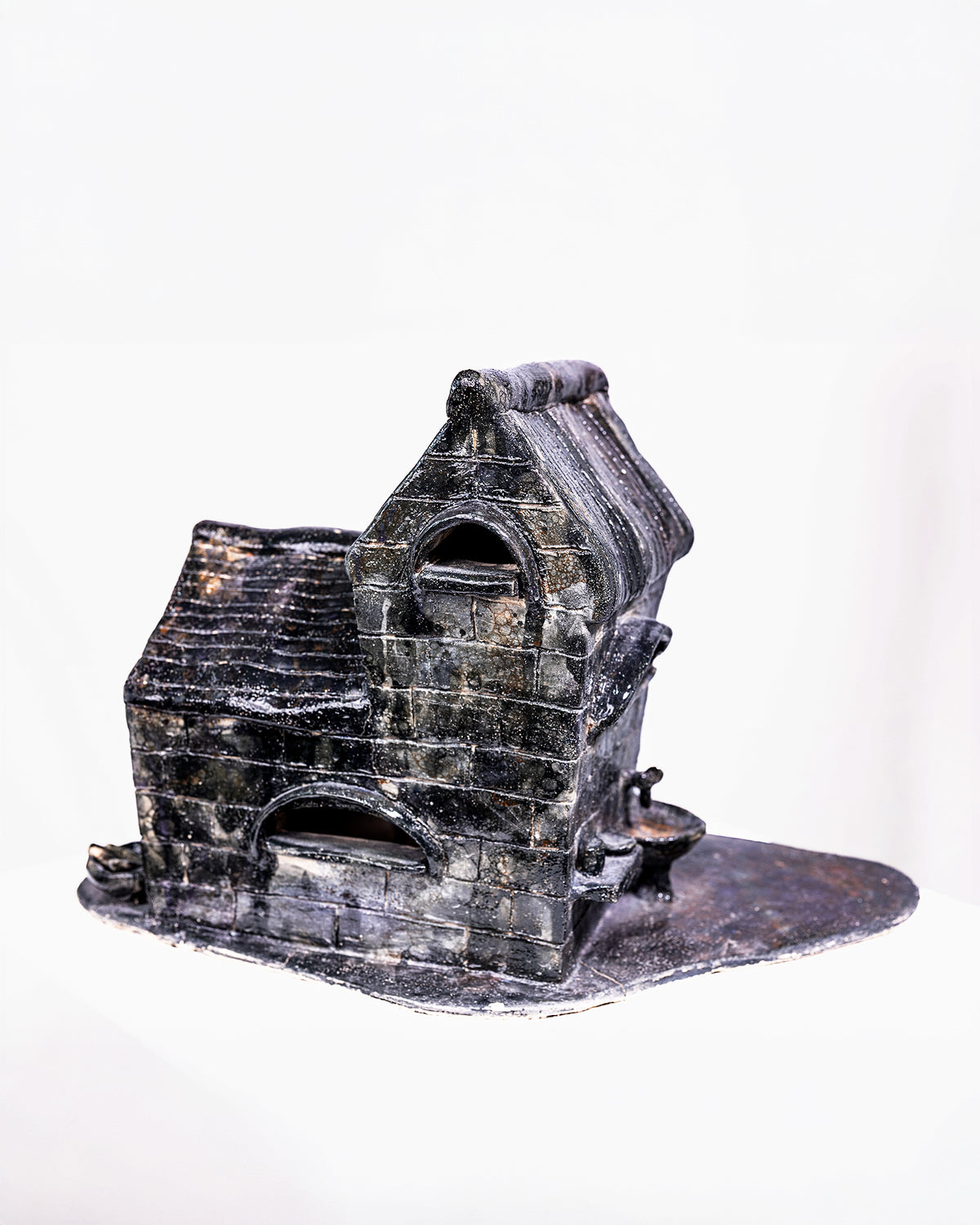A handcrafted ceramic sculpture titled "Dream," featuring a detailed miniature brick building with a dark black and grey glaze, accented by white highlights across its textured brickwork and ribbed pitched roof, set against a white background.