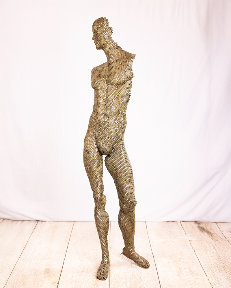A life-sized figurative sculpture of a standing nude male figure in profile with a tilted head, constructed entirely from welded dark iron nuts, standing against a plain white background.
