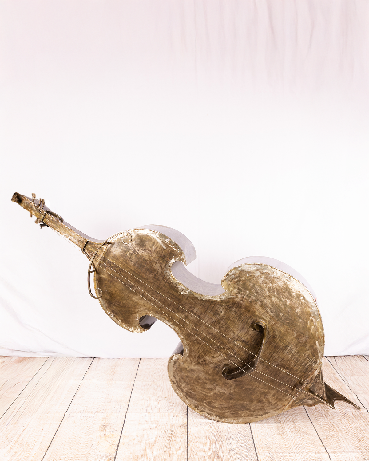 A life-sized double bass sculpture rendered entirely in dark iron, lying horizontally on its side with strings stretched tightly across the textured metal body, capturing a static tension against a neutral background.