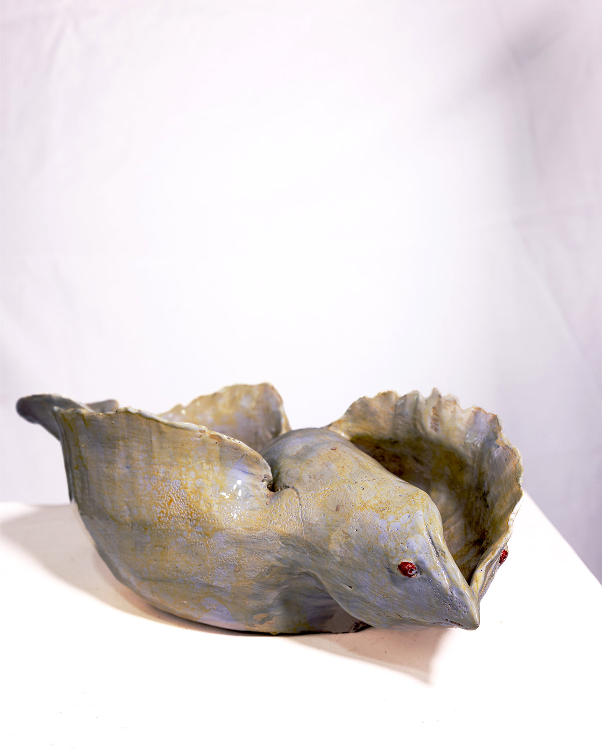 A sculptural ceramic planter shaped like a sleeping bird, featuring a textured, speckled glaze in muted gray, olive green, and gold tones, with small red eyes, set against a plain white background.