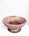 A handmade ceramic pedestal bowl with a textured, mottled glaze in earthy brown and beige tones, set against a plain white backdrop.