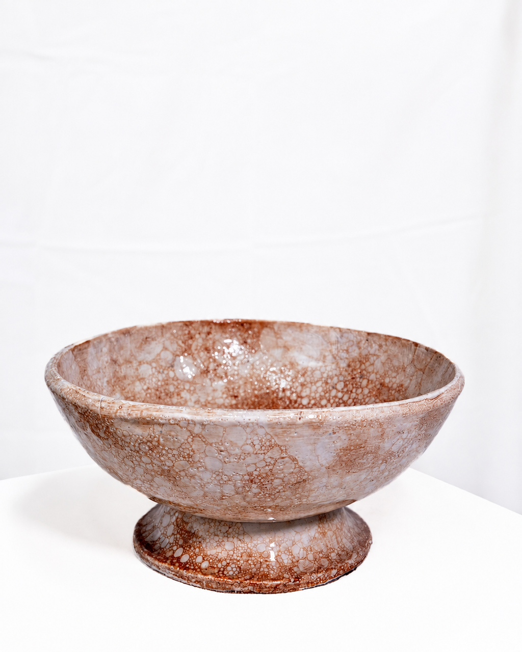 A handmade ceramic pedestal bowl with a mottled brown and beige glaze, set against a plain white background.
