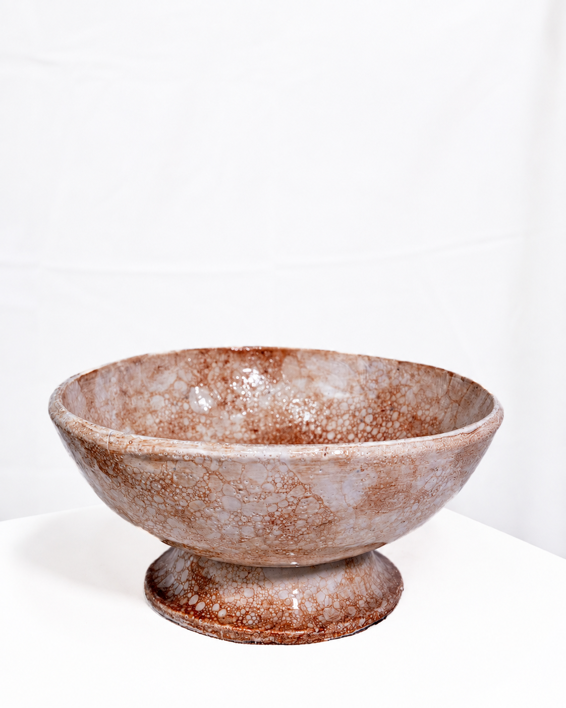 A handmade ceramic pedestal bowl with a mottled brown and beige glaze, set against a plain white background.