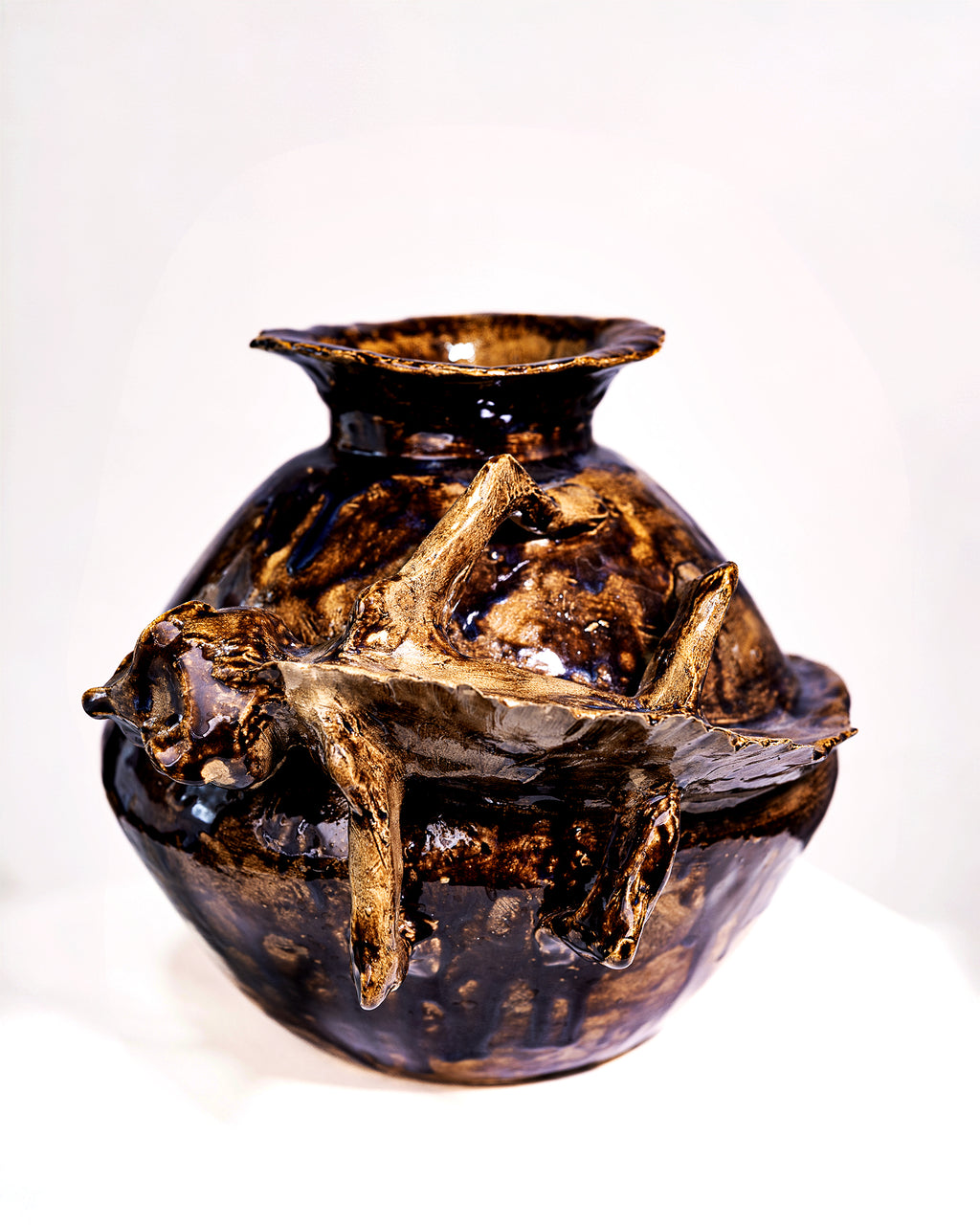 A handmade ceramic vase with a bulbous body, flared rim, and three abstract, branch-like protrusions on the front, covered in a glossy dark brown and black glaze with lighter tan highlights, photographed against a plain white background.