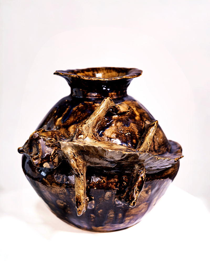 A handmade ceramic vase with a bulbous body, flared rim, and three abstract, branch-like protrusions on the front, covered in a glossy dark brown and black glaze with lighter tan highlights, photographed against a plain white background.